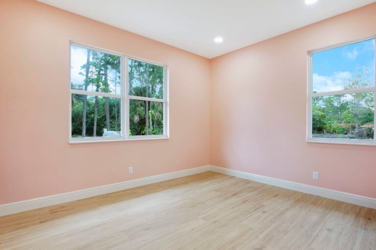An empty room with pink walls and wooden floors and two windows.
