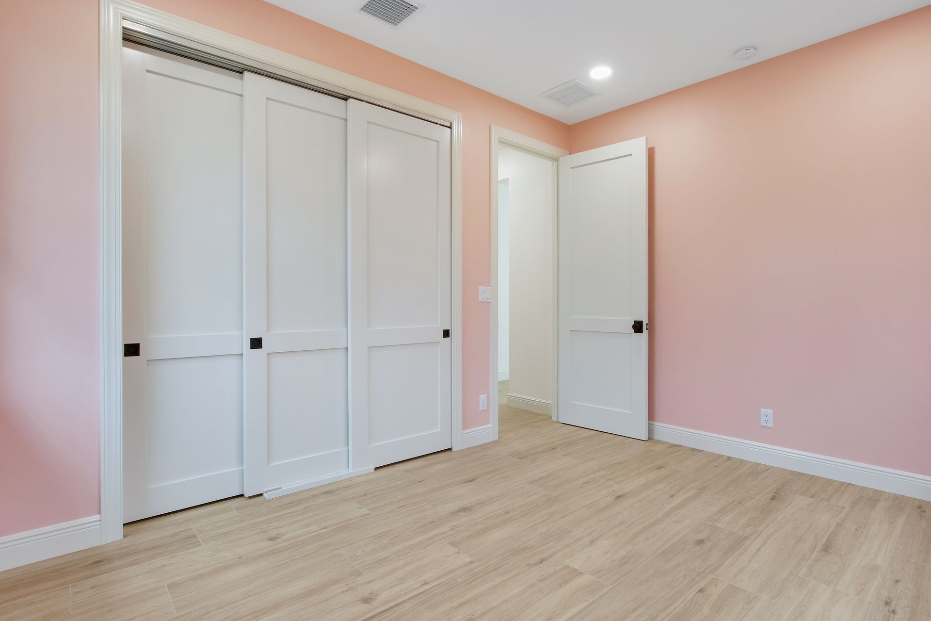 A bedroom with pink walls and white sliding doors.