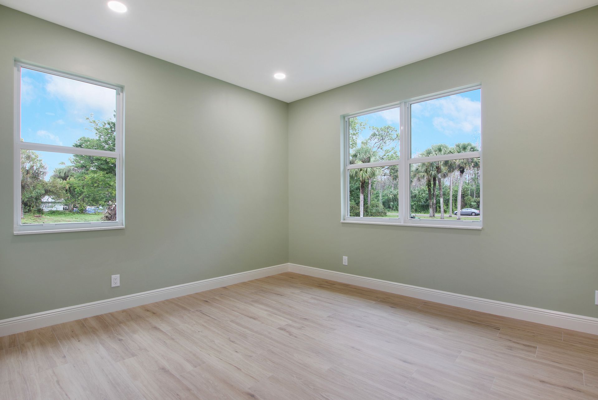An empty room with two windows and a wooden floor.