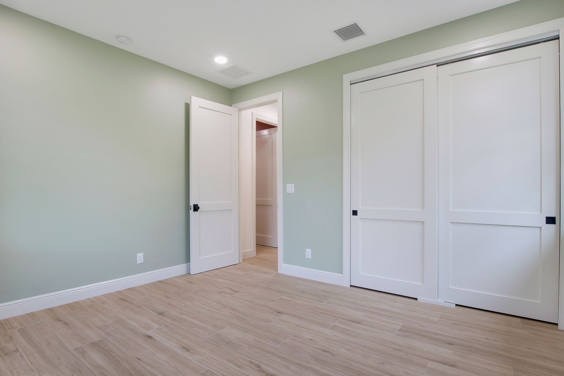 An empty bedroom with hardwood floors and white doors.