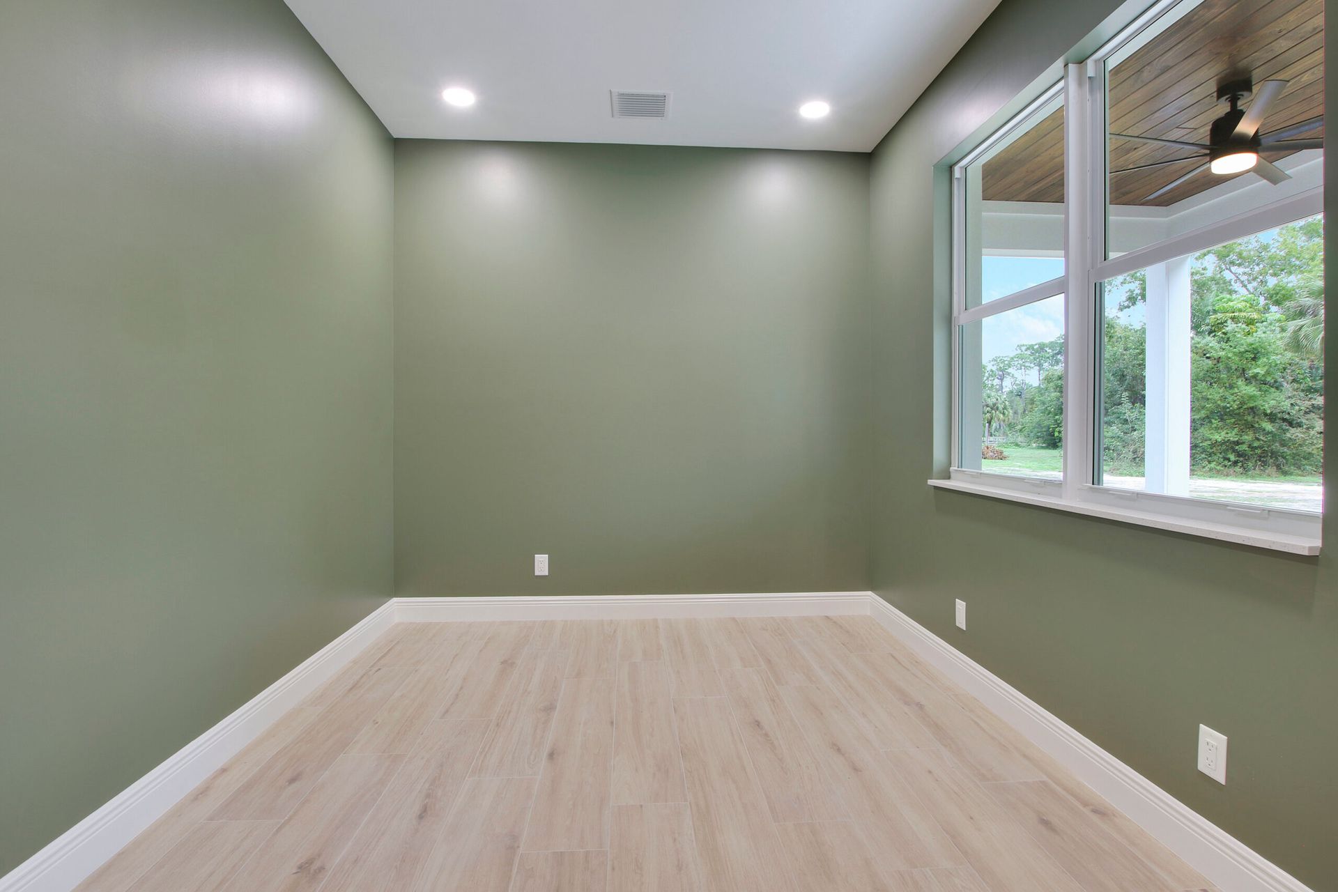 An empty room with green walls and a ceiling fan.