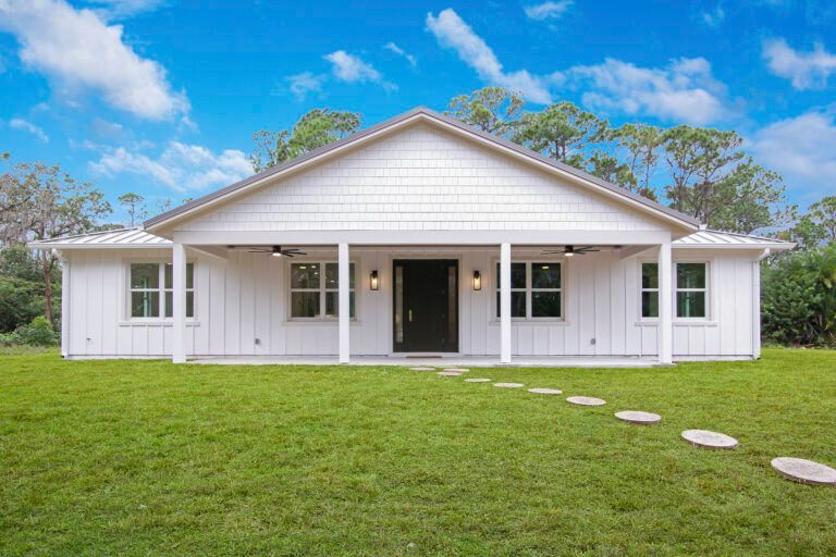 A white house with a porch and a lush green lawn in front of it.