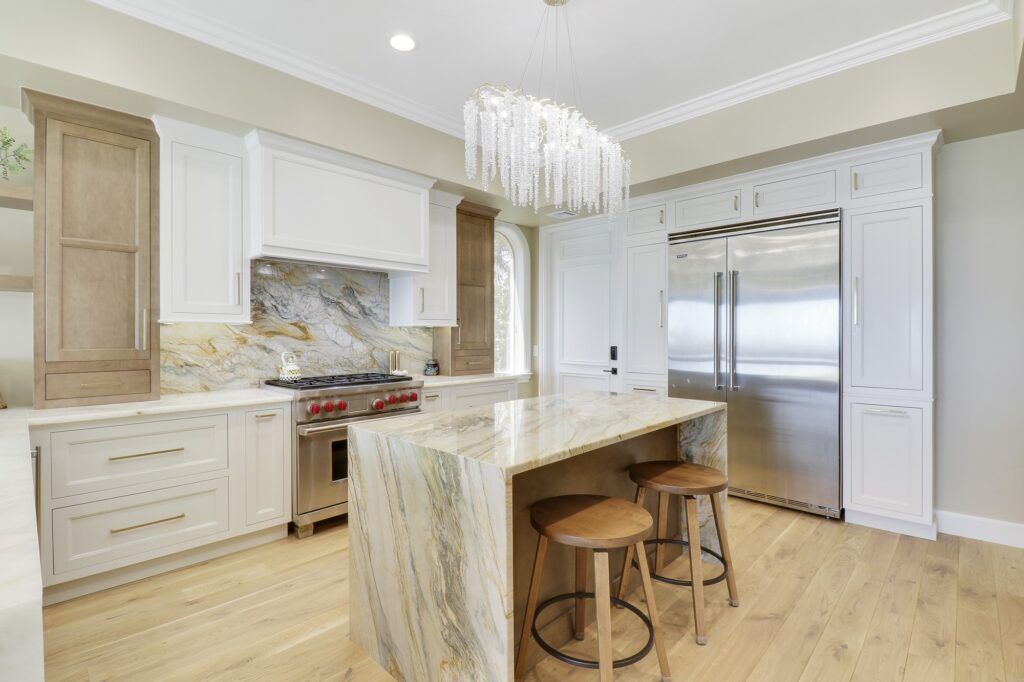 A kitchen with white cabinets , marble counter tops , stainless steel appliances and a large island.
