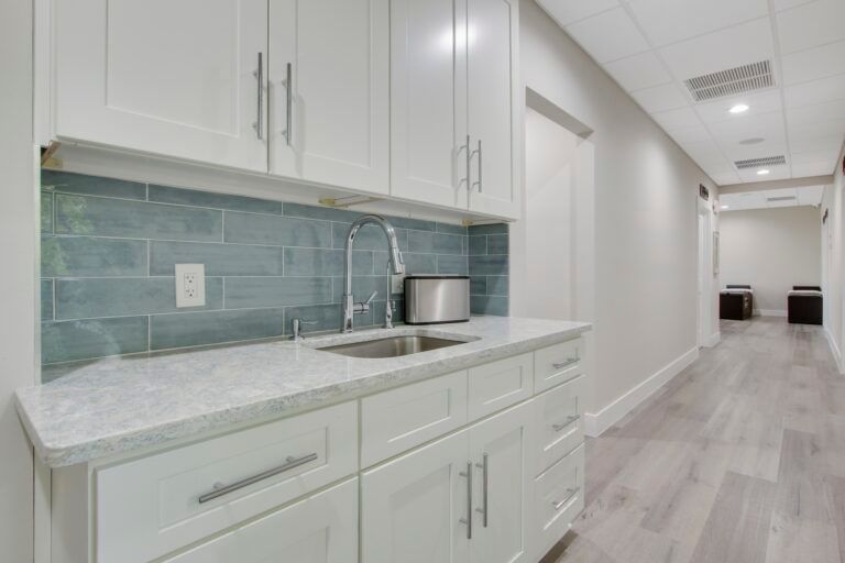 A kitchen with white cabinets and a sink in a hallway.