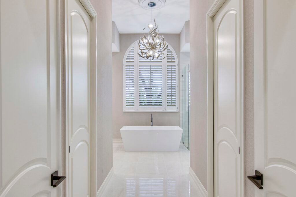 A hallway leading to a bathroom with a bathtub and a chandelier.