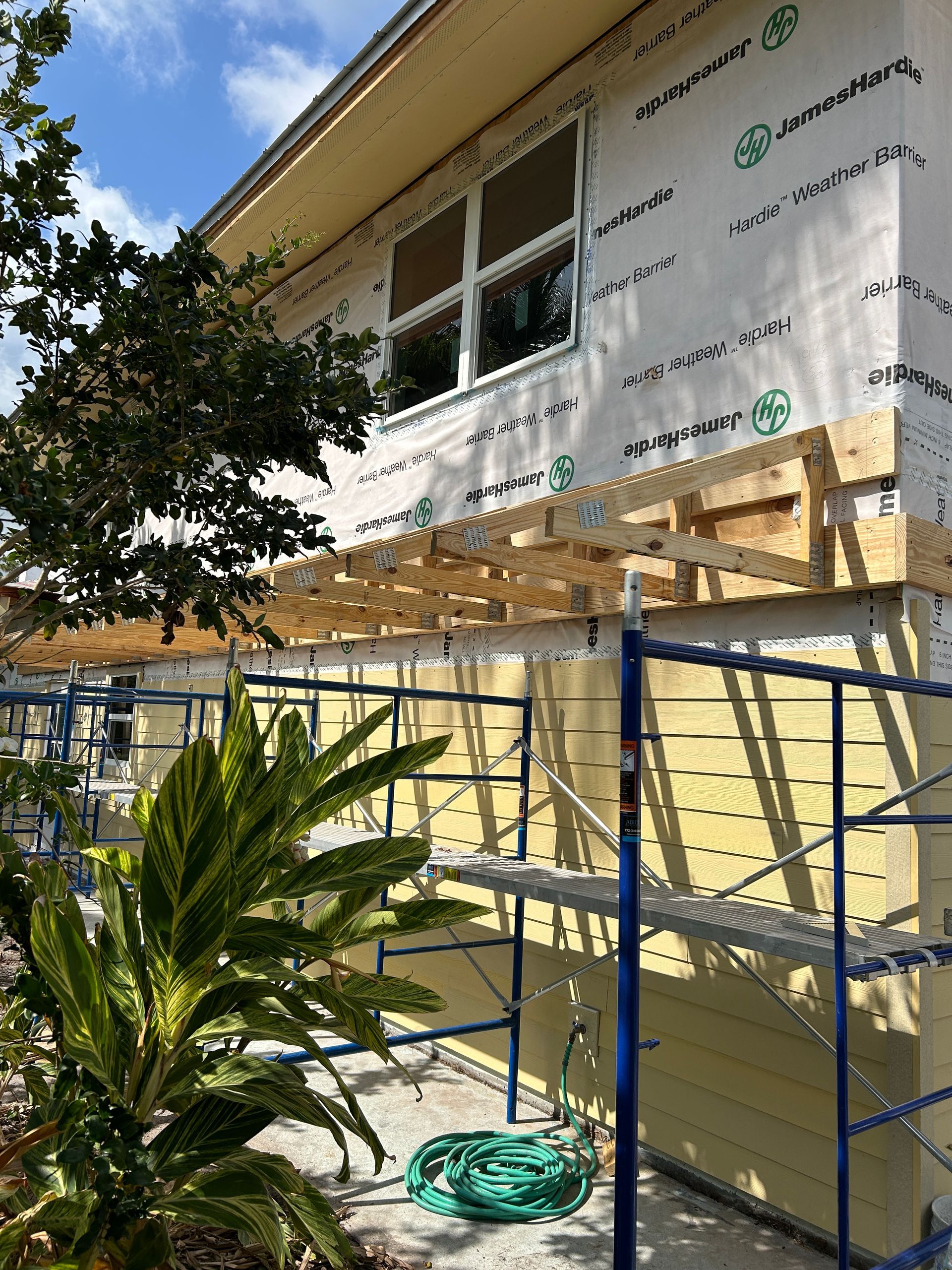 A house is being remodeled with scaffolding and a green hose.