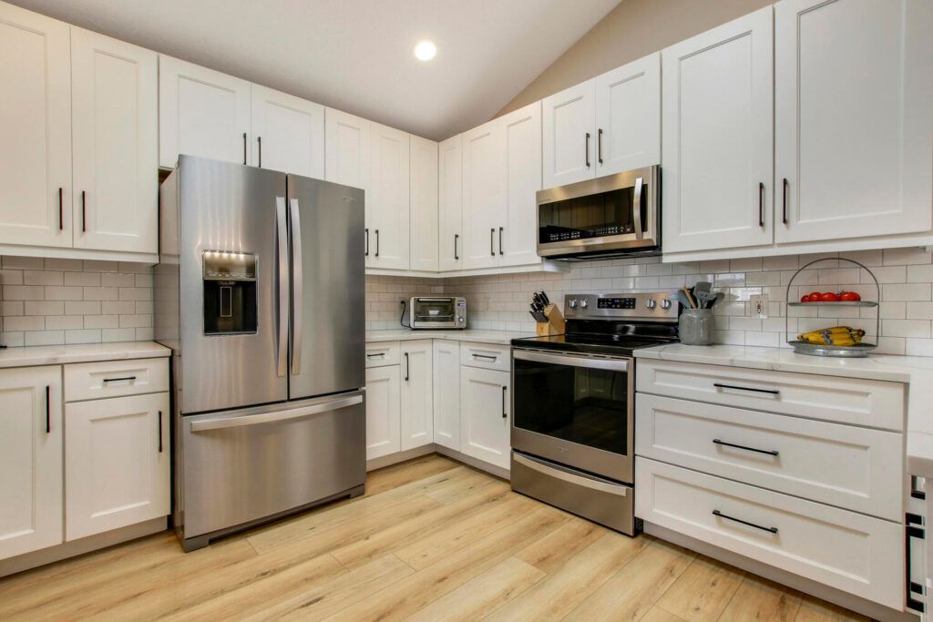A kitchen with white cabinets , stainless steel appliances , and hardwood floors.