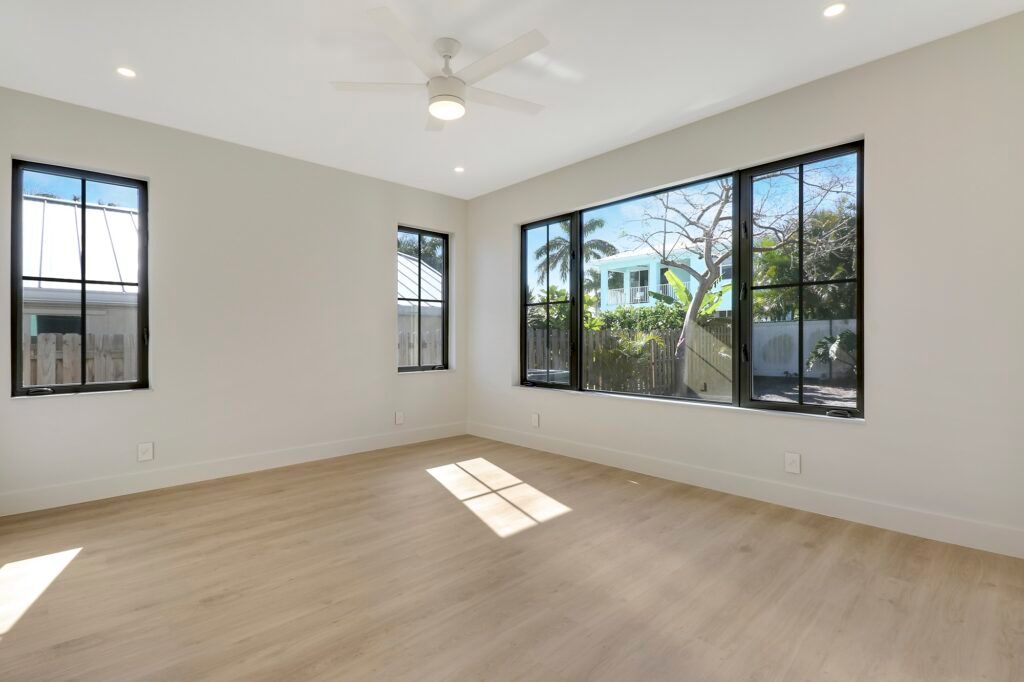 An empty living room with a lot of windows and a ceiling fan.