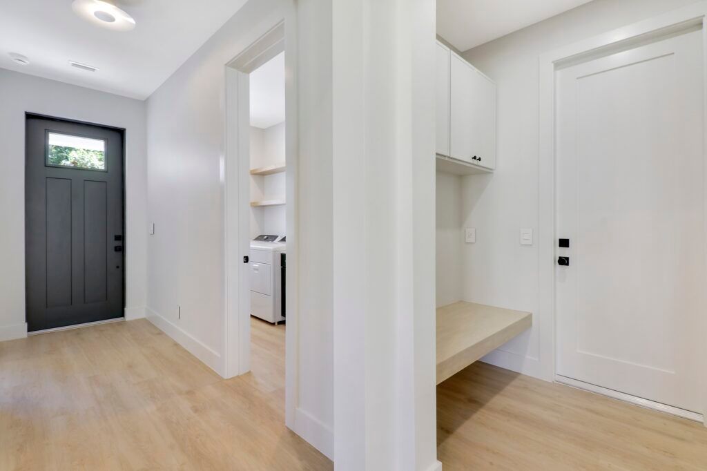 A hallway with hardwood floors and white walls leading to a laundry room.