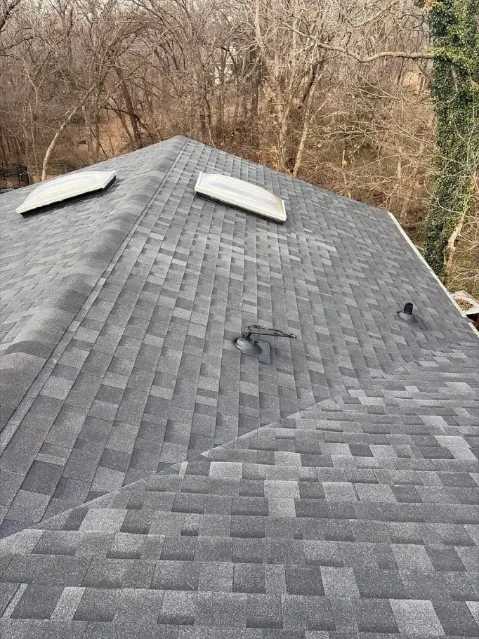 A high-angle view of a grey shingled residential roof with two skylights and two small dark vent pipes.