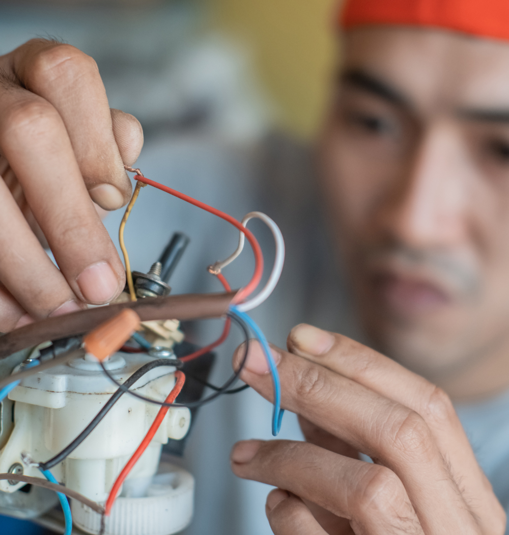 Man in red hat wiring electrical components, focused expression.