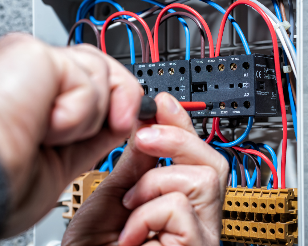 Person using a screwdriver on electrical wiring in a control panel, with red, blue, and black wires.