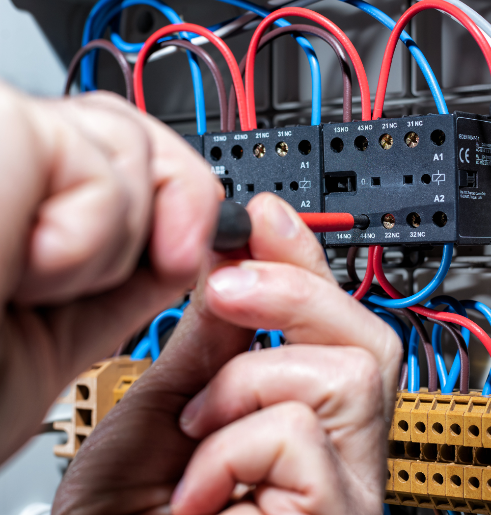 Electrician's hands wiring an electrical panel with red, blue, and black wires.