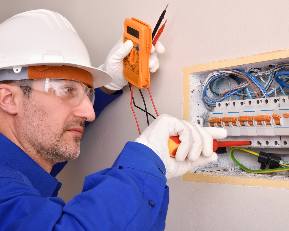 A man wearing a hard hat and gloves is working on an air conditioner.