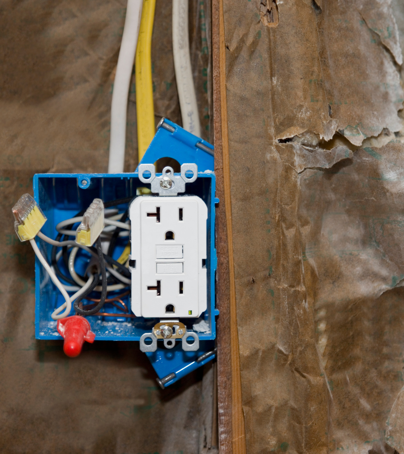 Blue electrical box with white outlet and wires on a damaged brown wall.