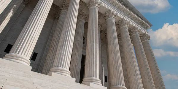 Exterior view of the US Supreme Court building, showing tall white columns against a blue sky with fluffy clouds.