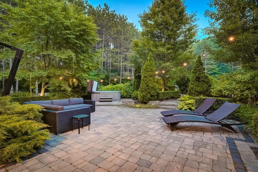 A patio with a couch , chairs and a hot tub surrounded by trees.