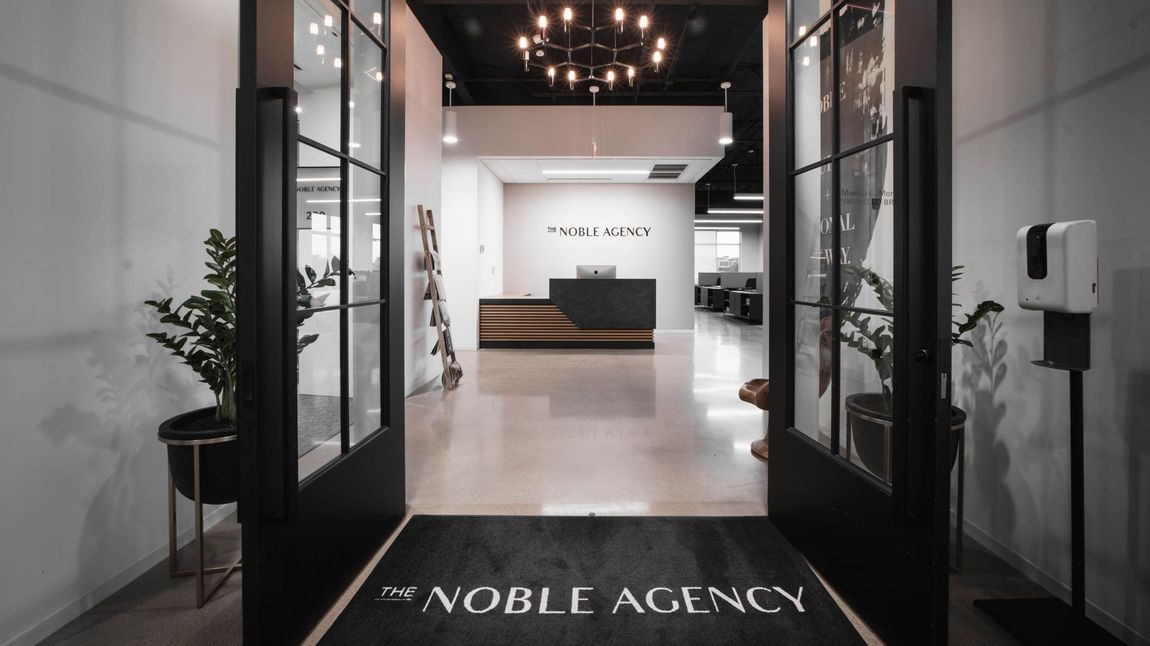 The Noble Agency office entrance with black framed glass doors, reception desk