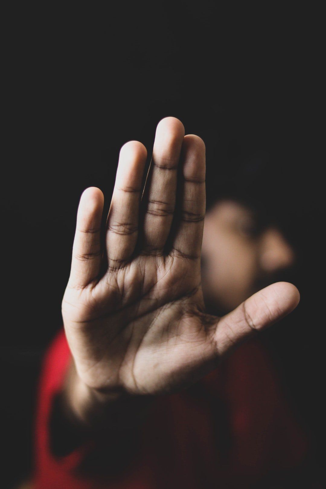 Outstretched hand, palm facing forward in a stop gesture, dark background.
