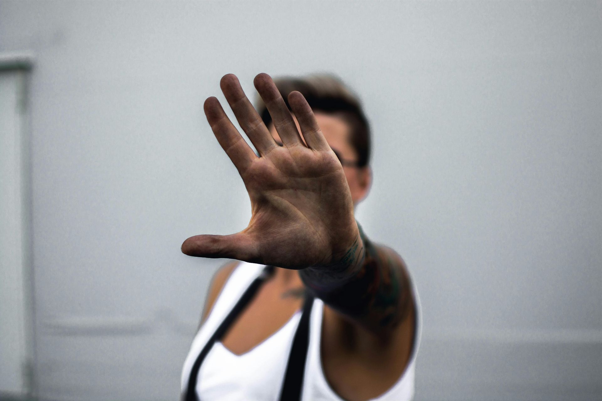Person with arm extended, hand open in a stop gesture, with tattoos visible.