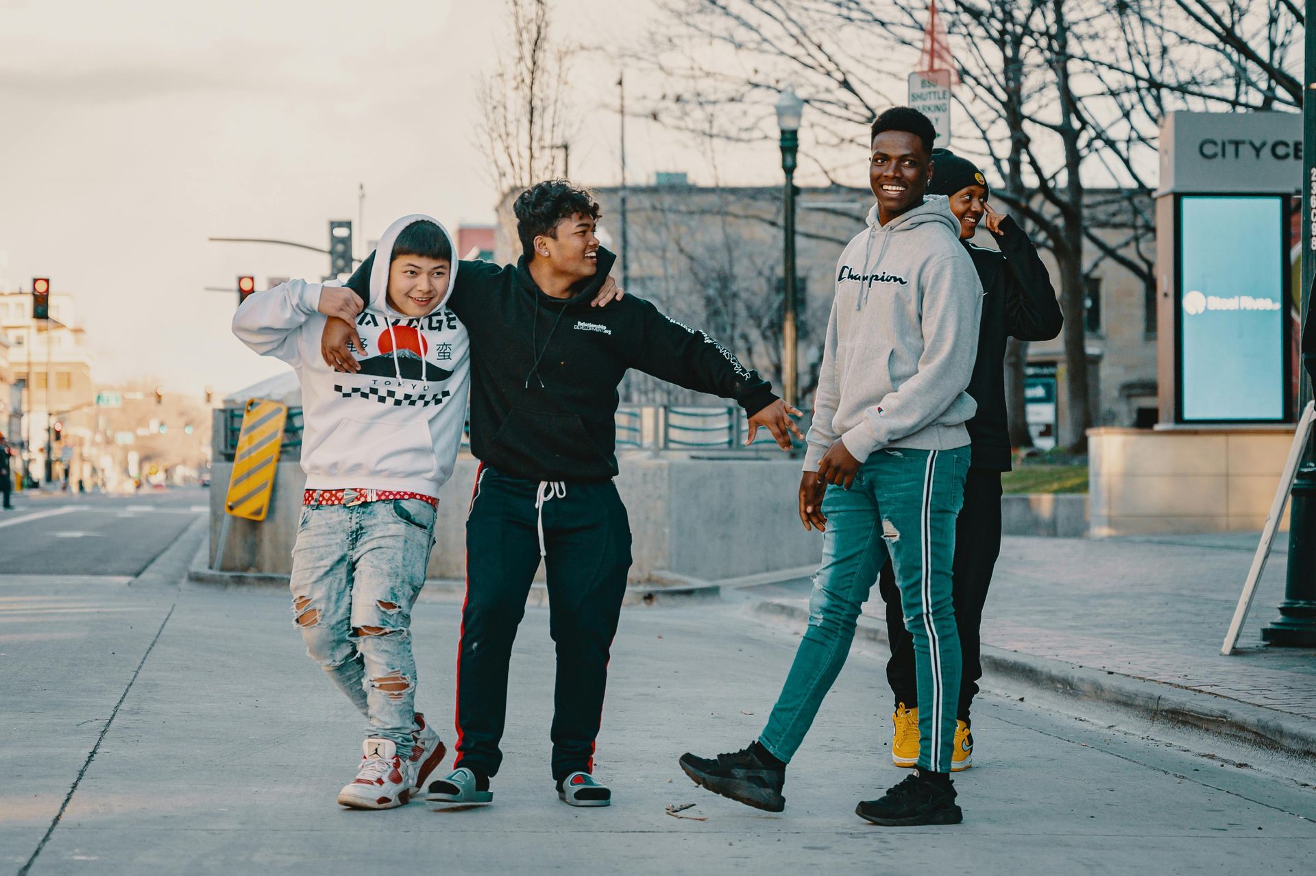 Four people smiling and posing on a city street. Buildings and crosswalks in background.
