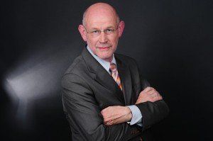 Ein Mann in Anzug und Krawatte steht mit verschränkten Armen da.