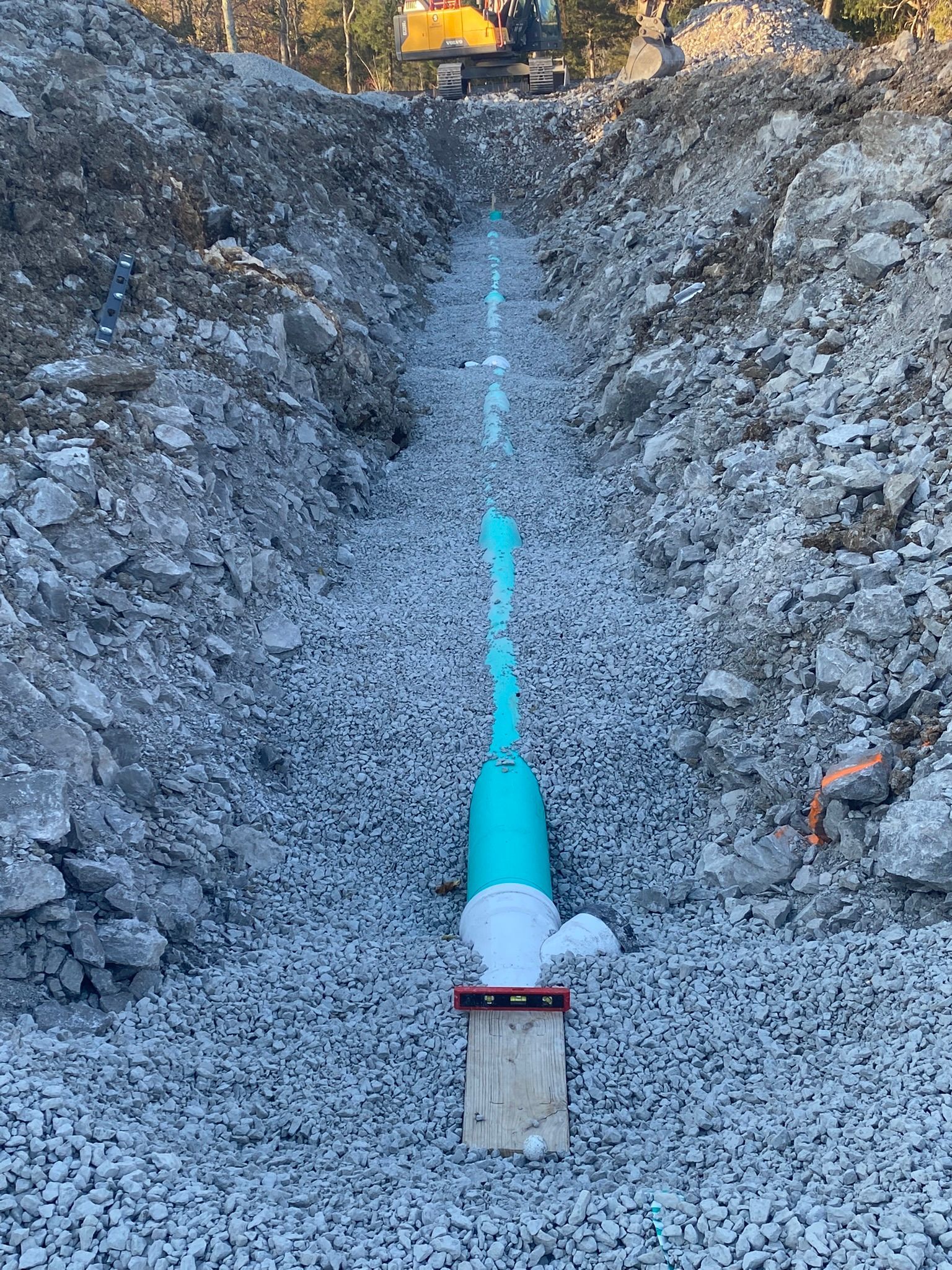 A blue pipe is being installed in a gravel trench.