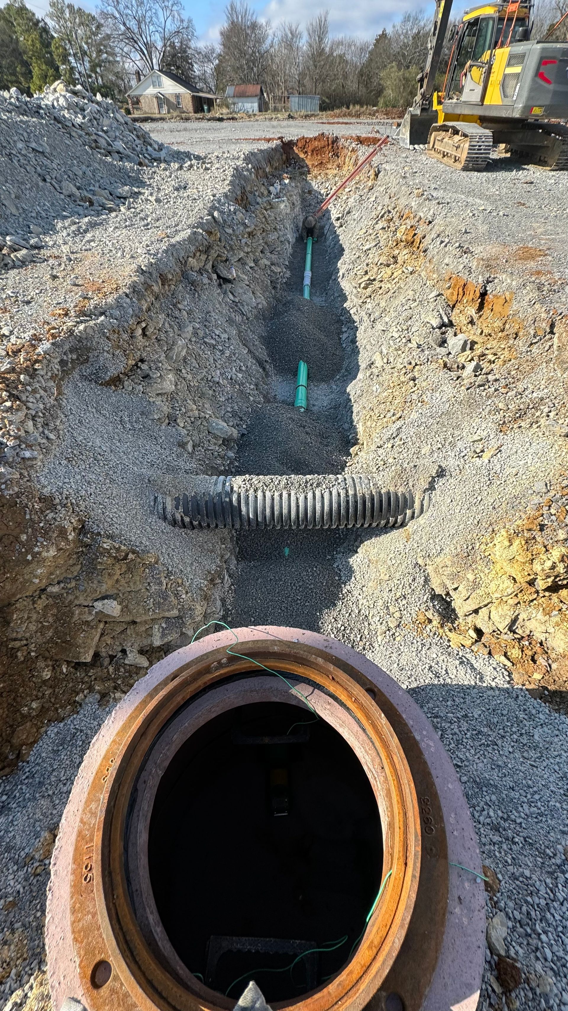 A manhole cover is sitting in the dirt next to a pipe.