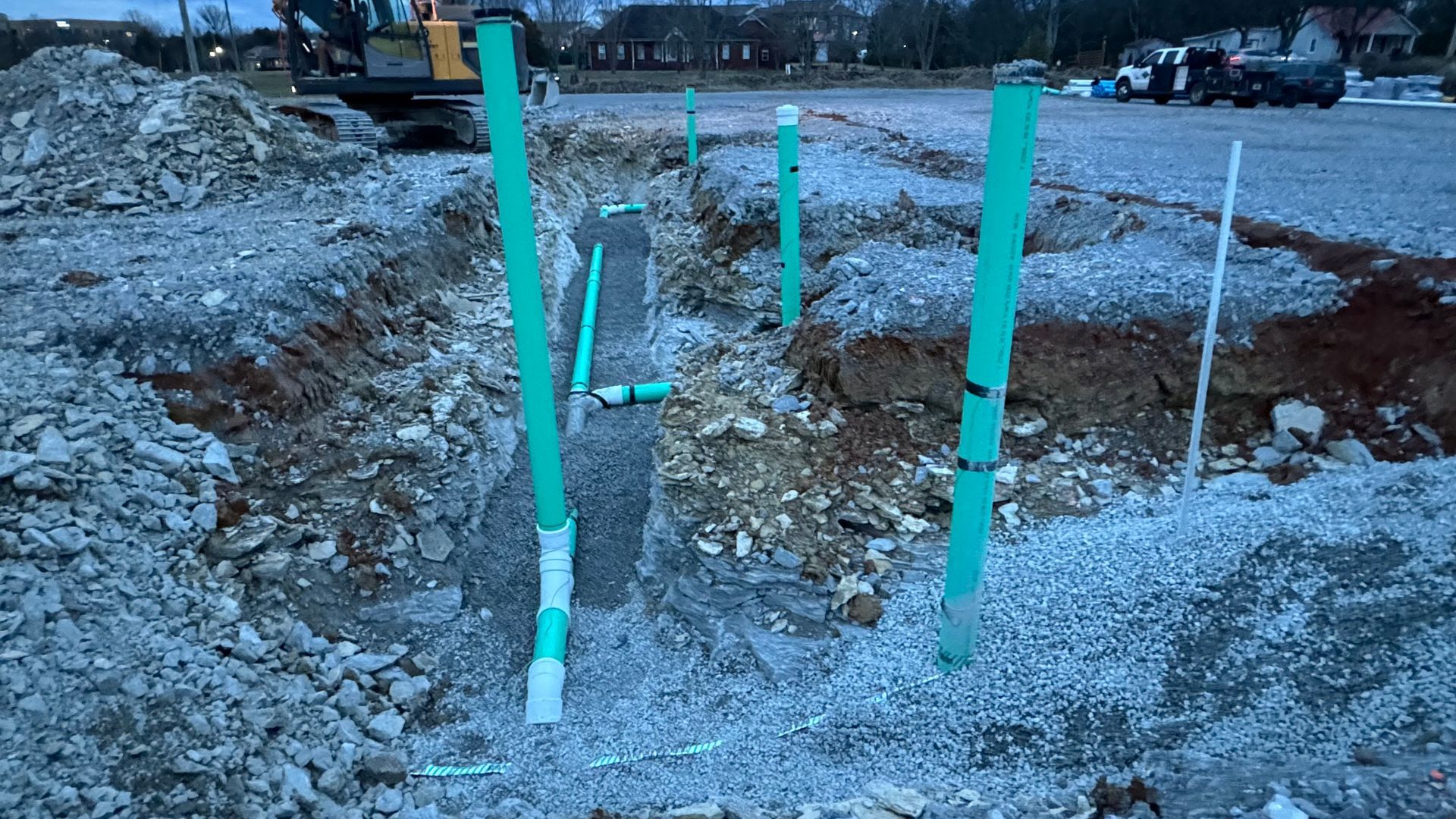 A construction site with green pipes in the dirt and a bulldozer in the background.