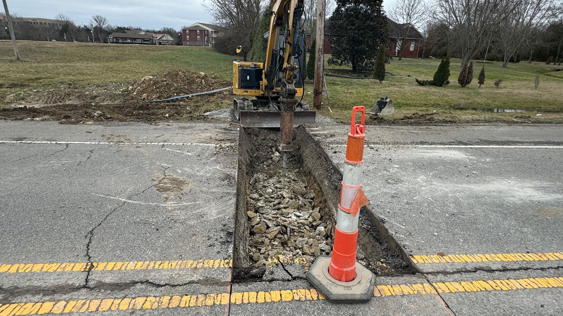 A yellow excavator is digging a hole in the side of the road.