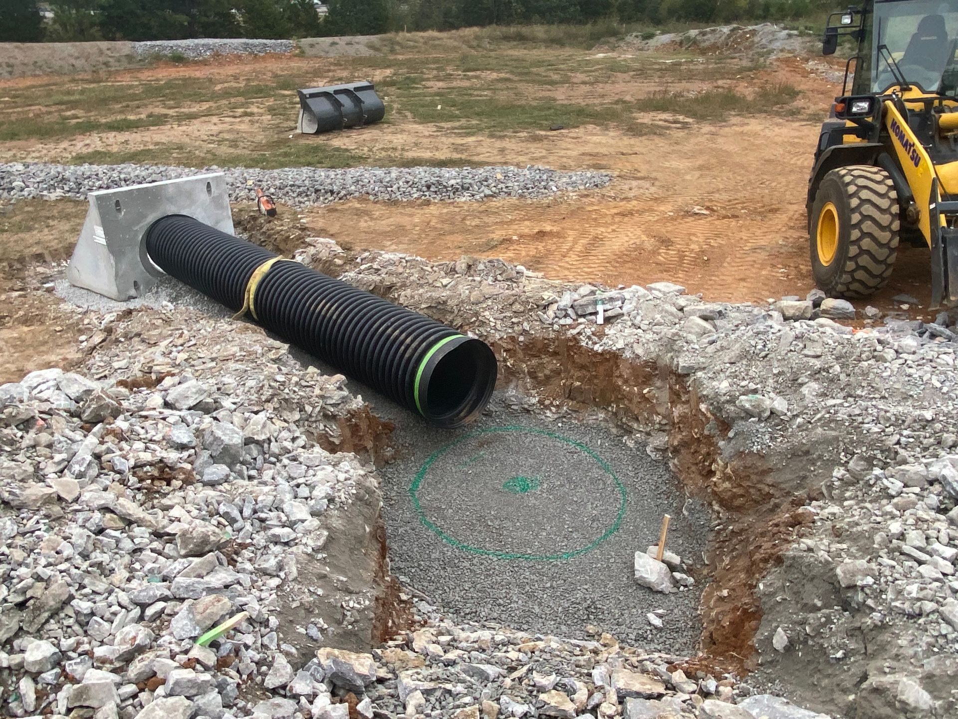 A yellow tractor is digging a hole in the dirt next to a large black pipe.