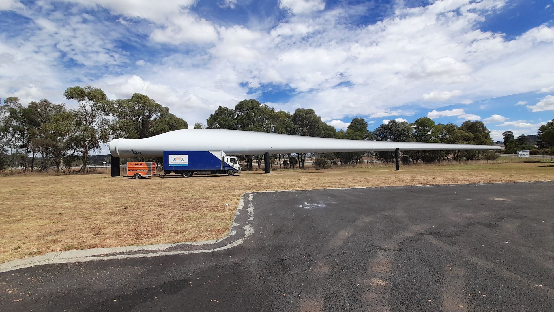 A long white-roofed building beside a paved lot and dry grassy field under a cloudy sky — TJ Removals and Storage in Wagga Wagga, NSW