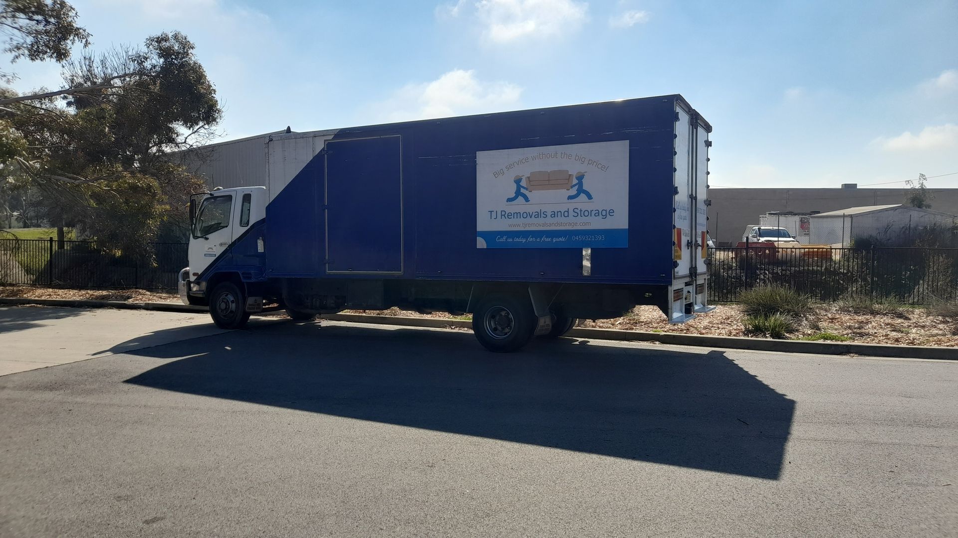 Blue delivery truck parked on a sunny street beside houses and trees — TJ Removals and Storage in Wagga Wagga, NSW