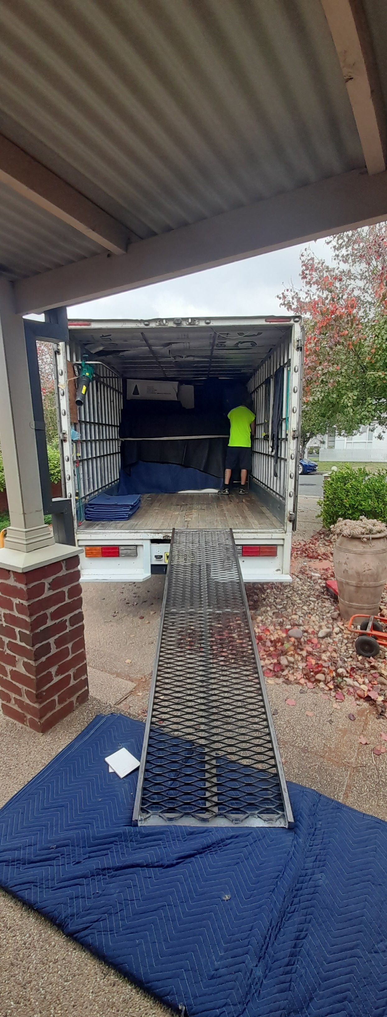 Ramp leading to moving truck parked under a carport, with a worker in a neon safety vest inside — TJ Removals and Storage in Wagga Wagga, NSW