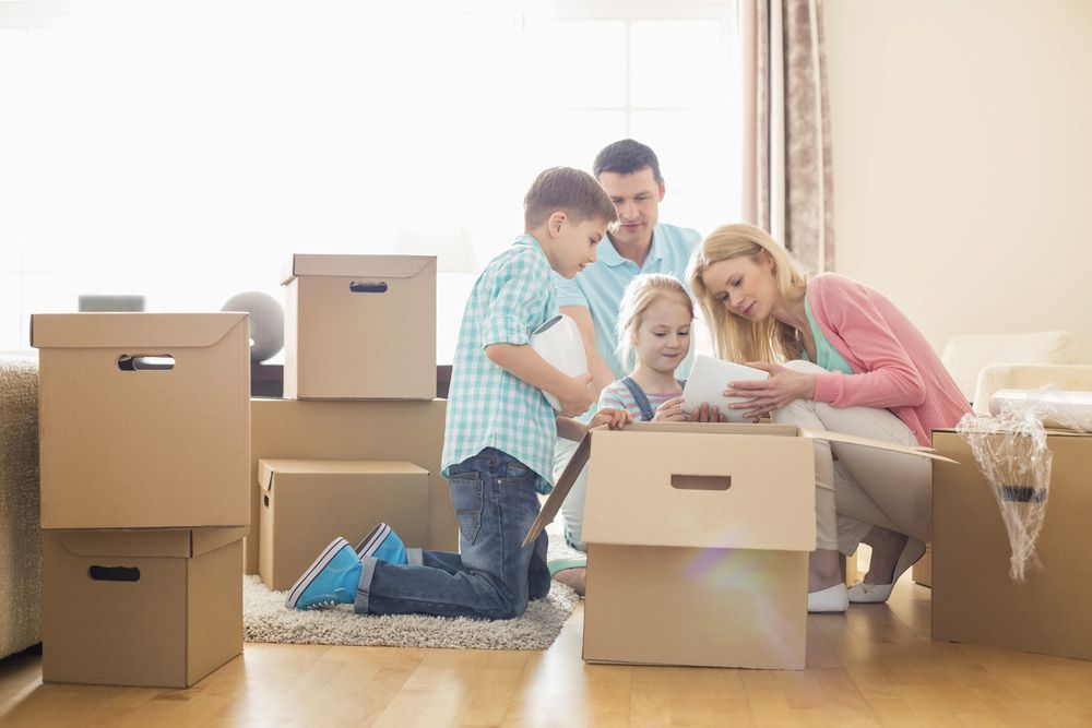 A Family is Sitting on the Floor in a Living Room Surrounded by Cardboard Boxes — TJ Removals and Storage in Wagga Wagga, NSW