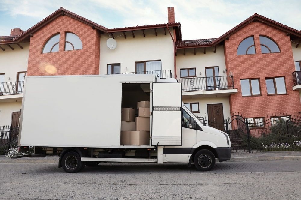A White Moving Truck is Parked in Front of a Large House — TJ Removals and Storage in Junee, NSW