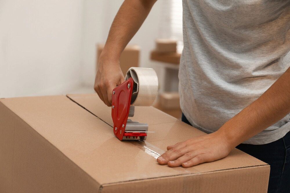 A Person is Taping a Cardboard Box With Tape — TJ Removals and Storage in Temora, NSW