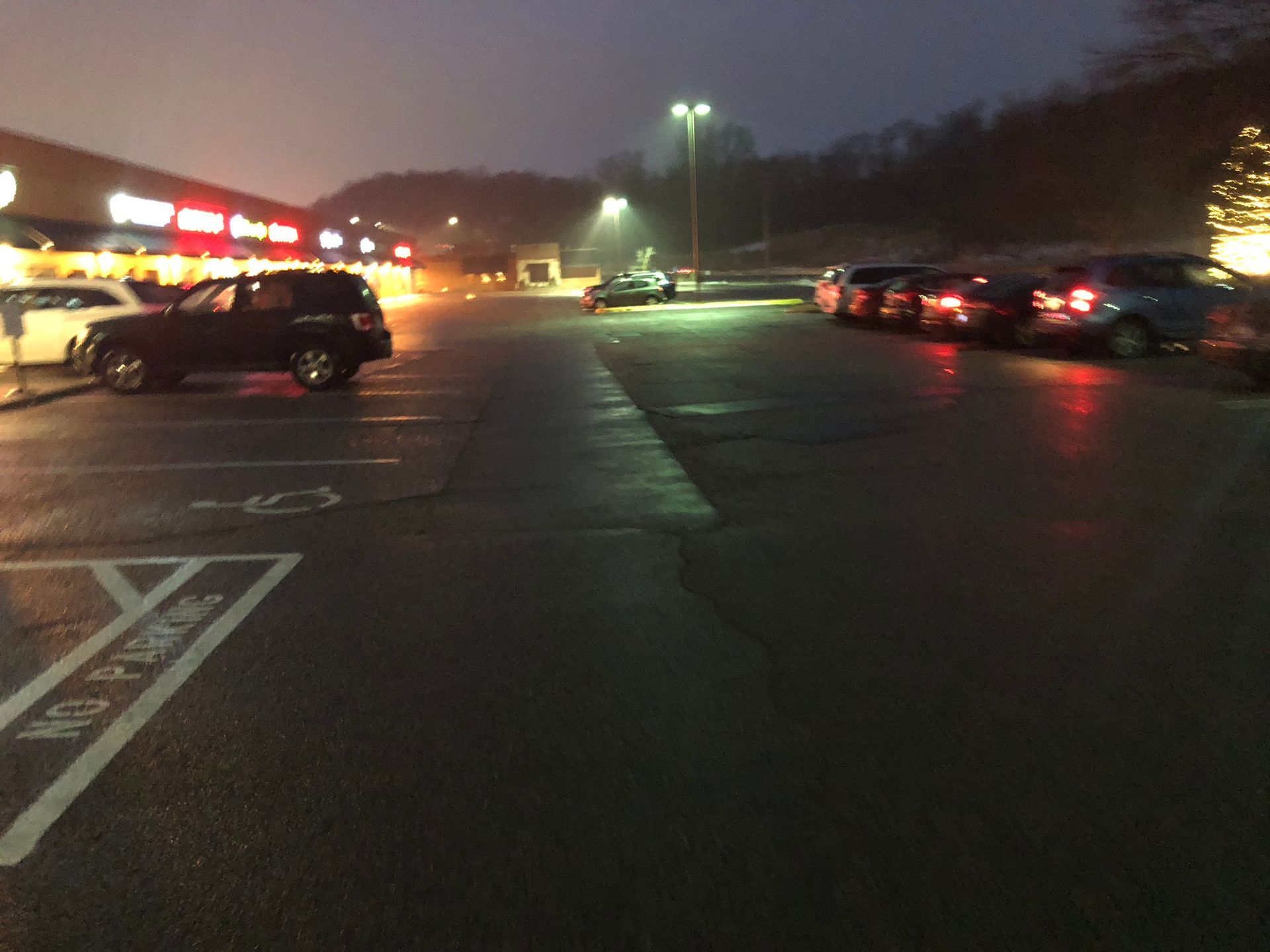 A row of cars are parked in a parking lot at night