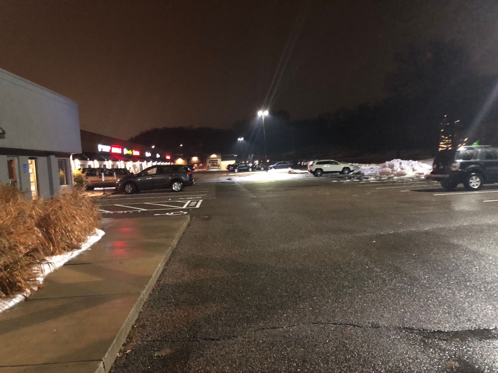 A parking lot with cars parked in front of a building at night