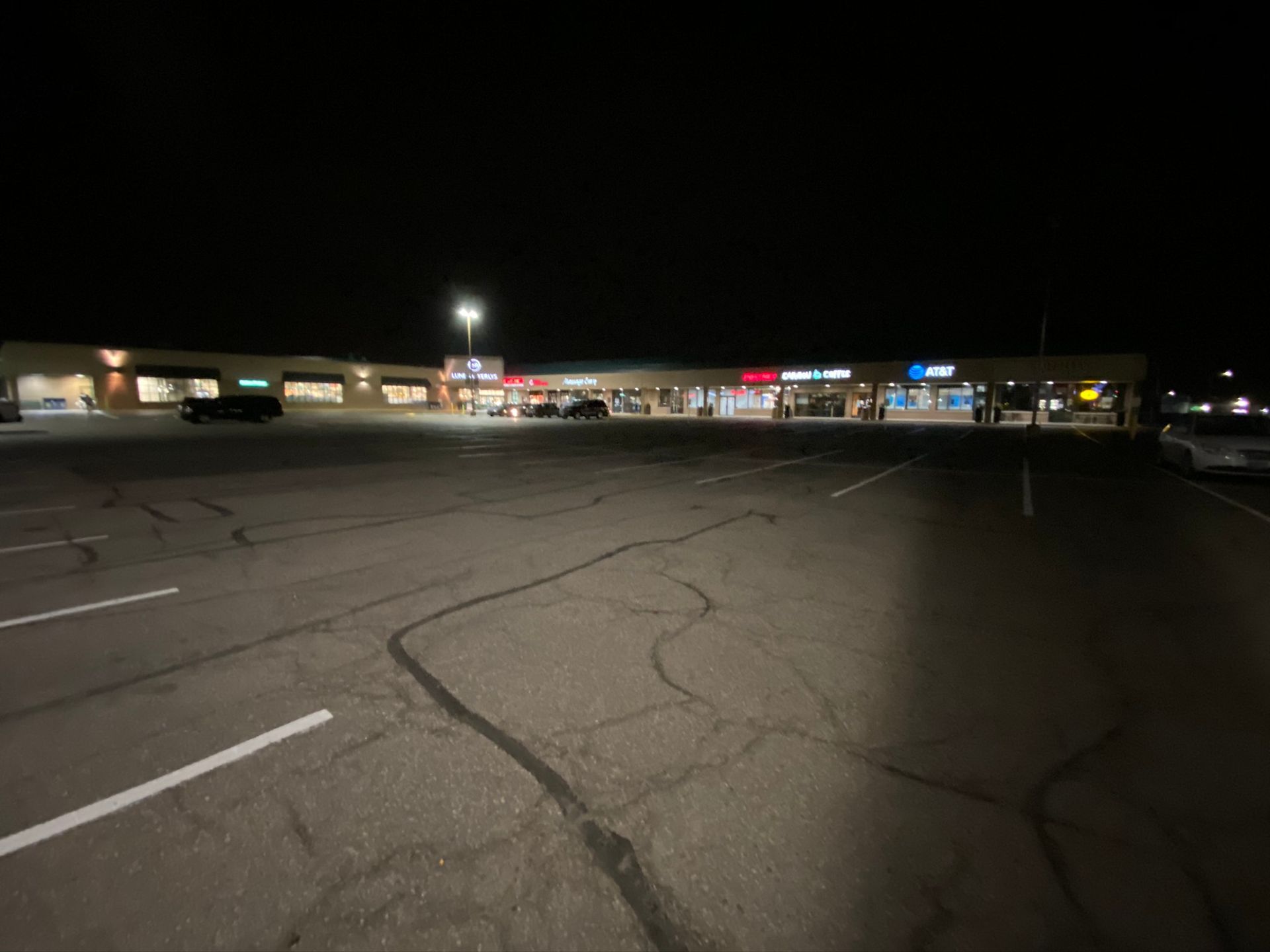 A parking lot in front of a shopping center at night.