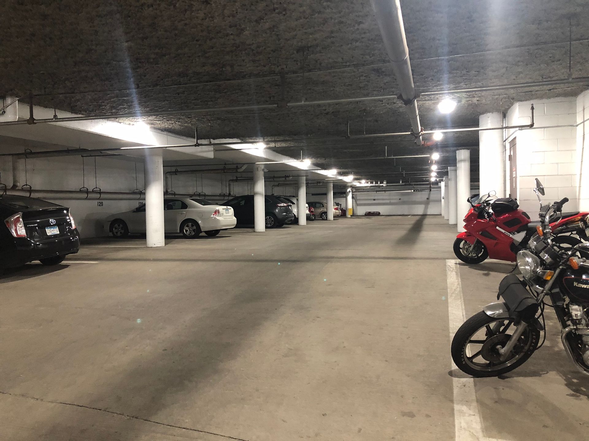 A parking garage with cars and motorcycles parked in it