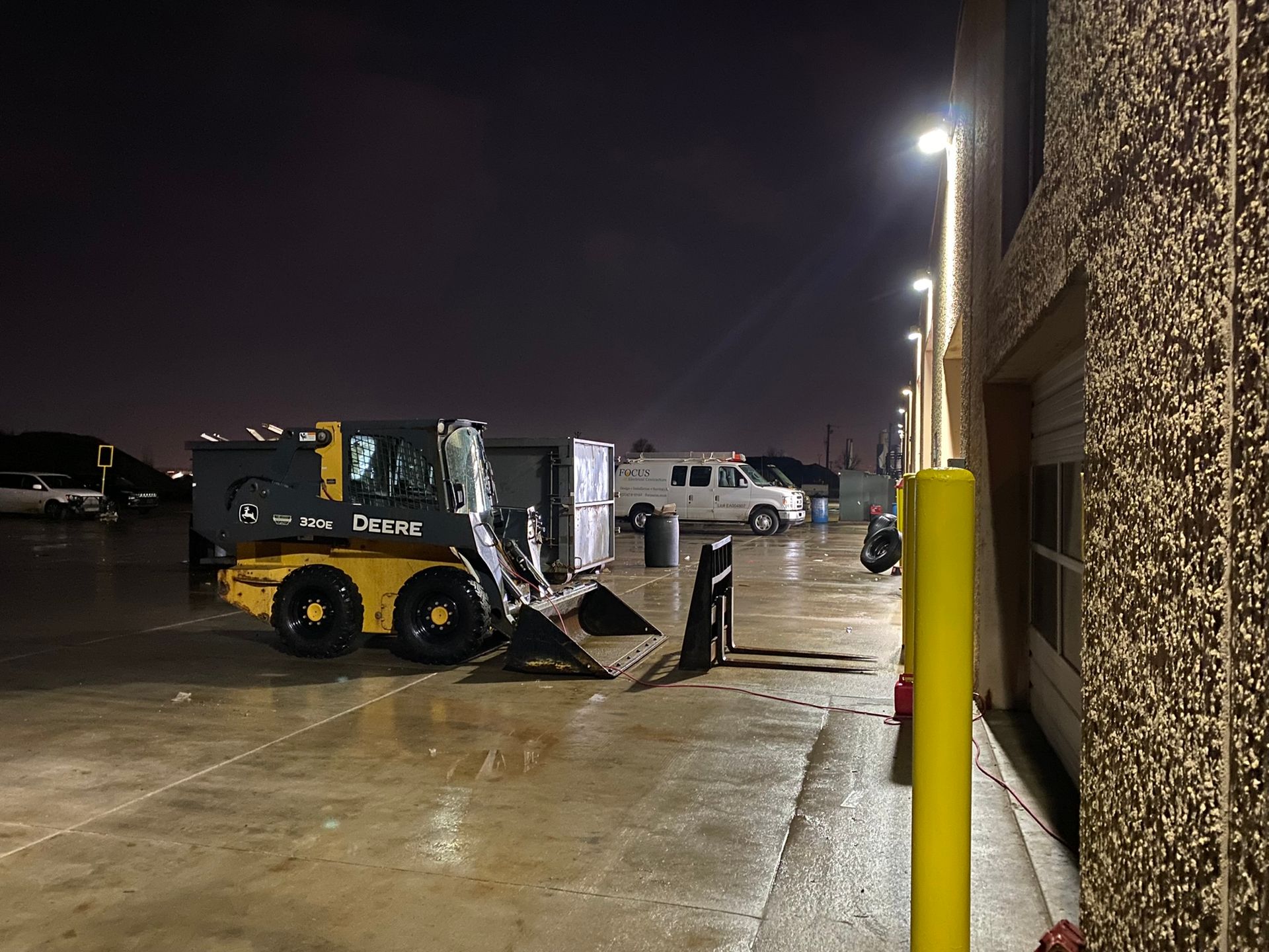 A yellow tractor is parked in a parking lot at night.