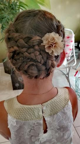 Une petite fille porte un chignon tressé avec une fleur dans les cheveux.