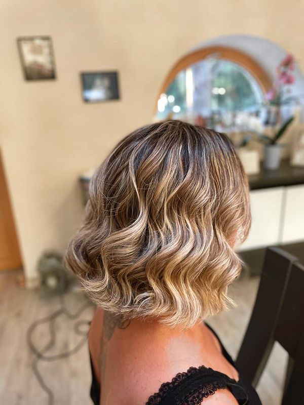 Une femme aux cheveux courts et ondulés est assise devant un miroir.