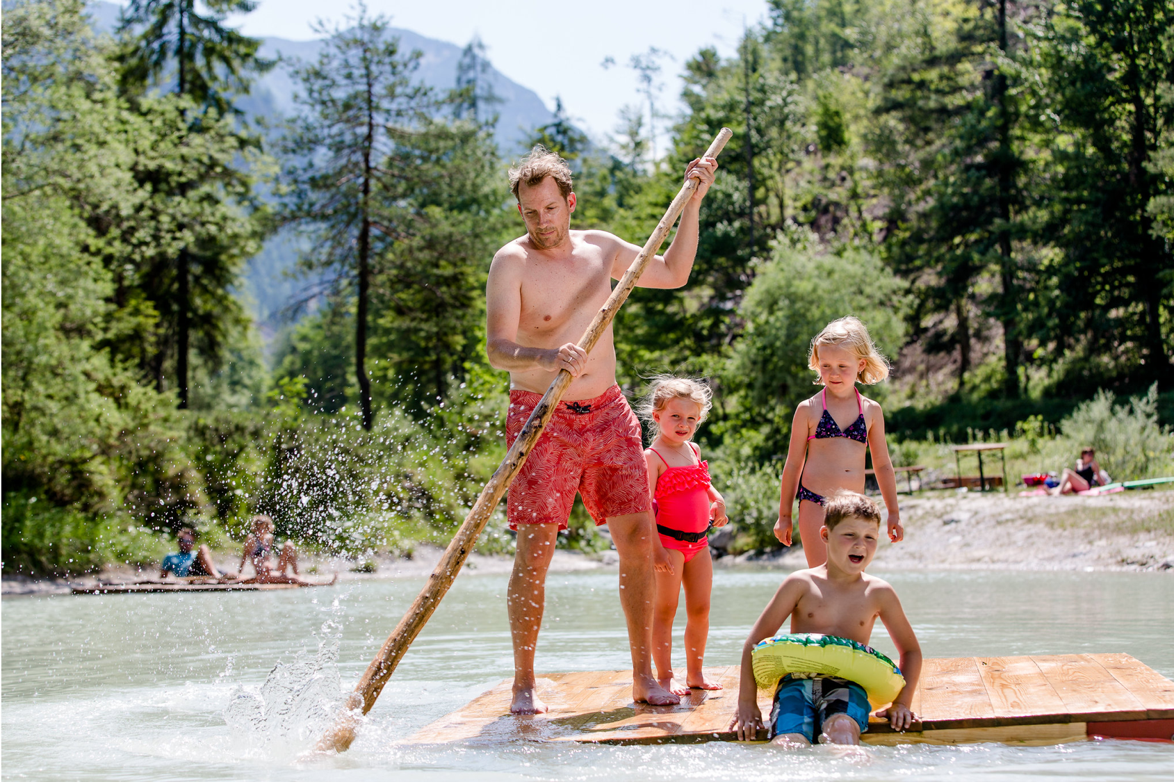 summer family fun a man stands on a wooden raft with three children