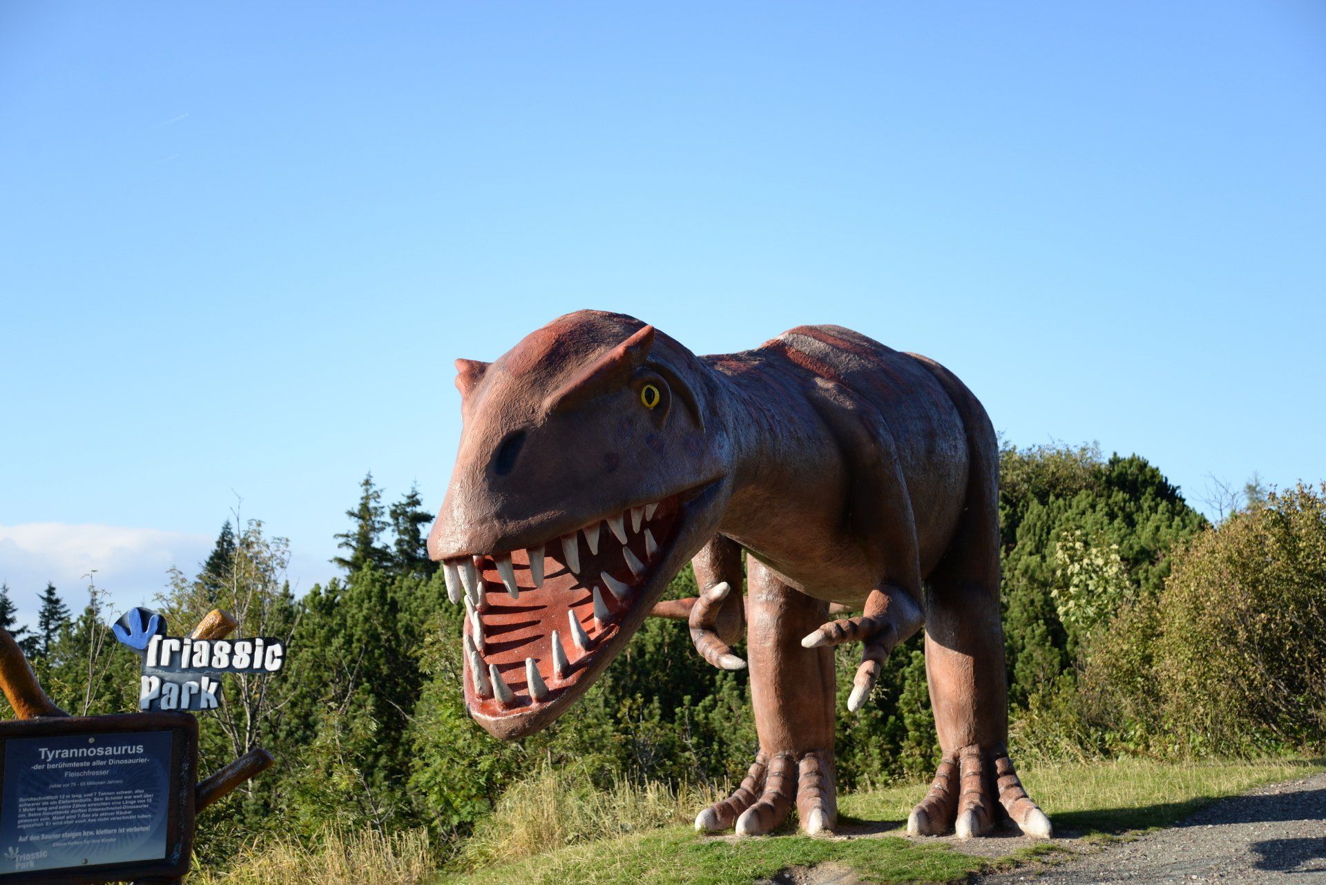 Große braune Tyrannosaurus Rex-Statue mit geöffnetem Maul auf einem Hügel in der Nähe des Schildes „Triassic Park“.