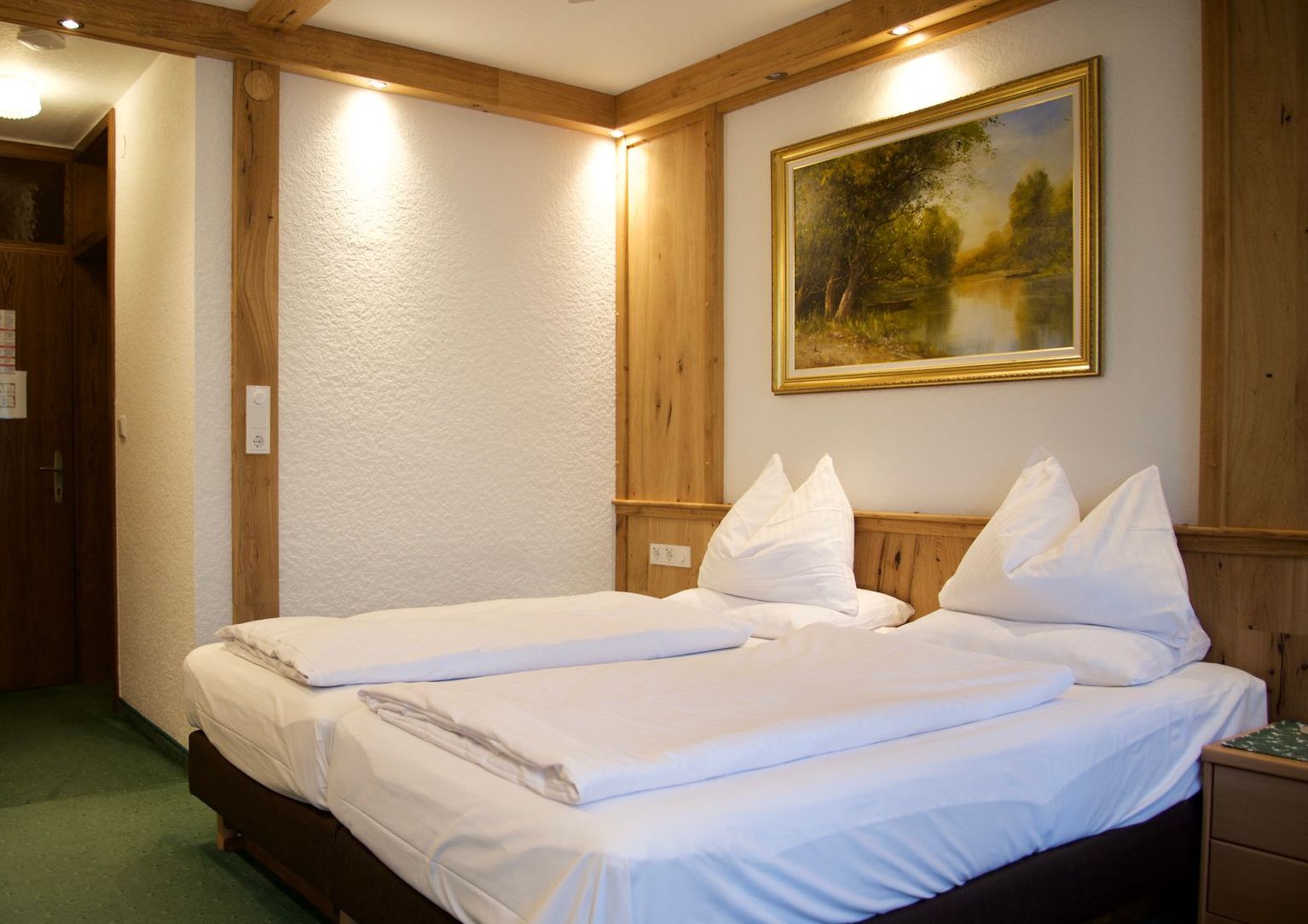 Ein Hotelzimmer mit einem Doppelbett, zwei Kissen pro Person, moderne und praktische Einrichtung, einem Gemälde an der Wand und Holzelementen.