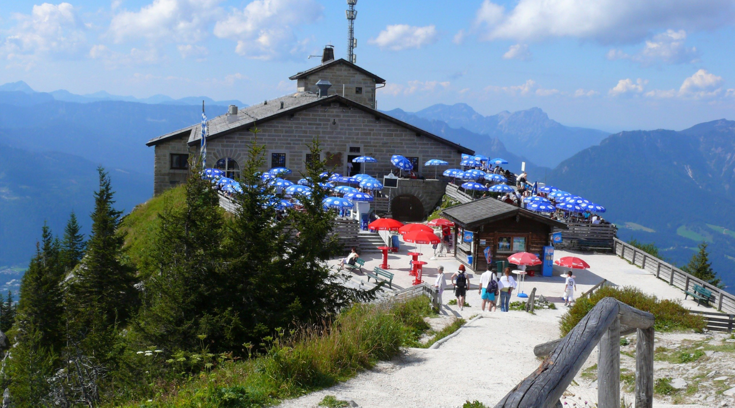 Das Kehlsteinhaus: Ein Gebäude mit blauen Sonnenschirmen auf einem Berggipfel mit Blick auf die Berge, Menschen im Freien.