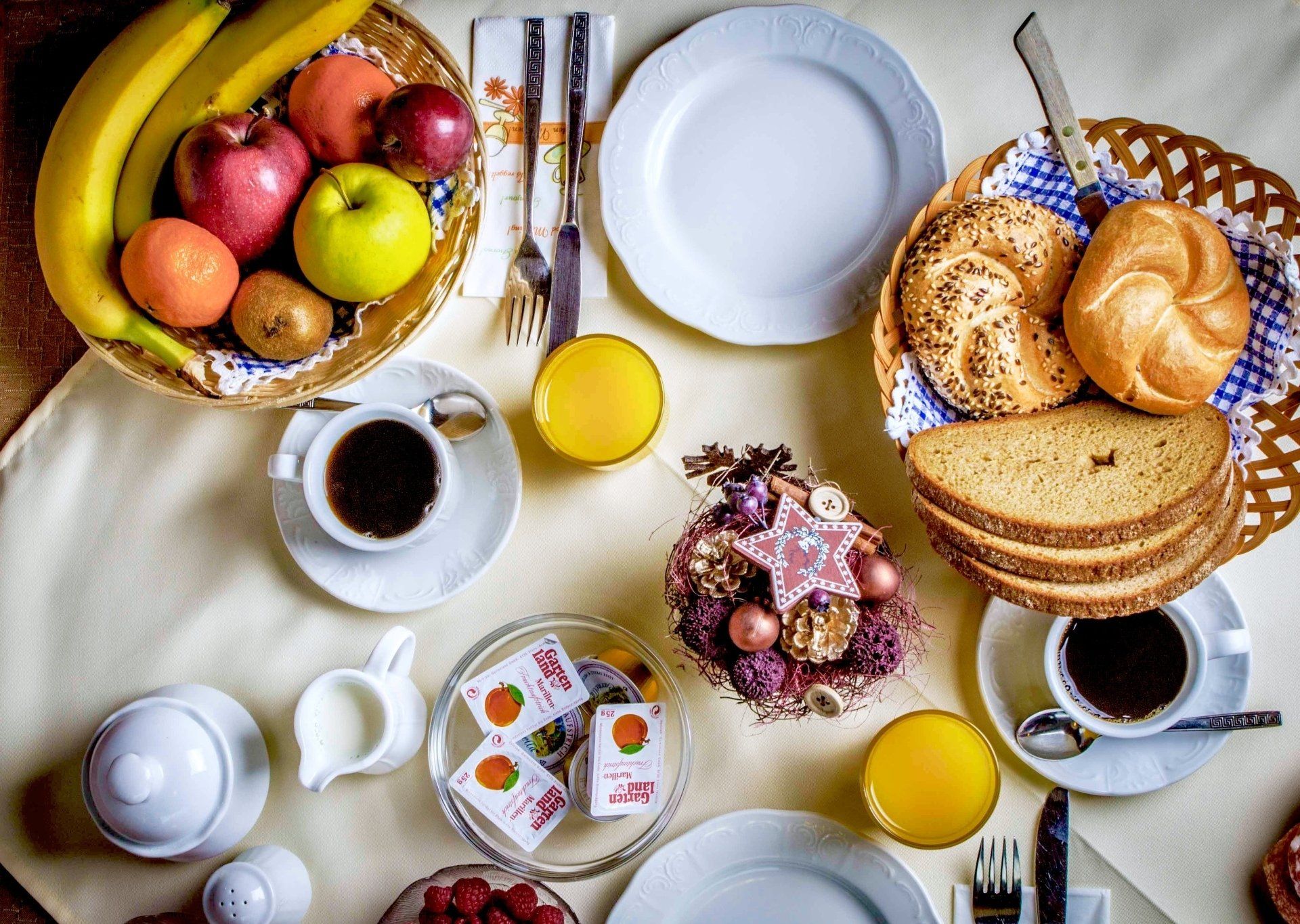 Frühstückstisch mit Obst, Brot, Kaffee, Saft, Marmeladen und Tellern.