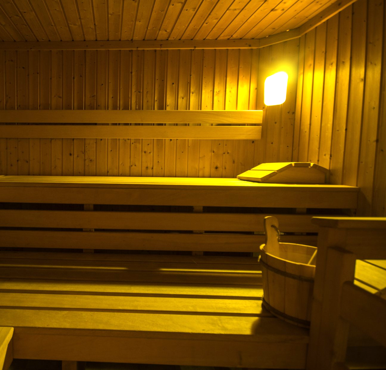 Saunainterieur aus Holz mit Bänken, Eimer und Deckenleuchte.